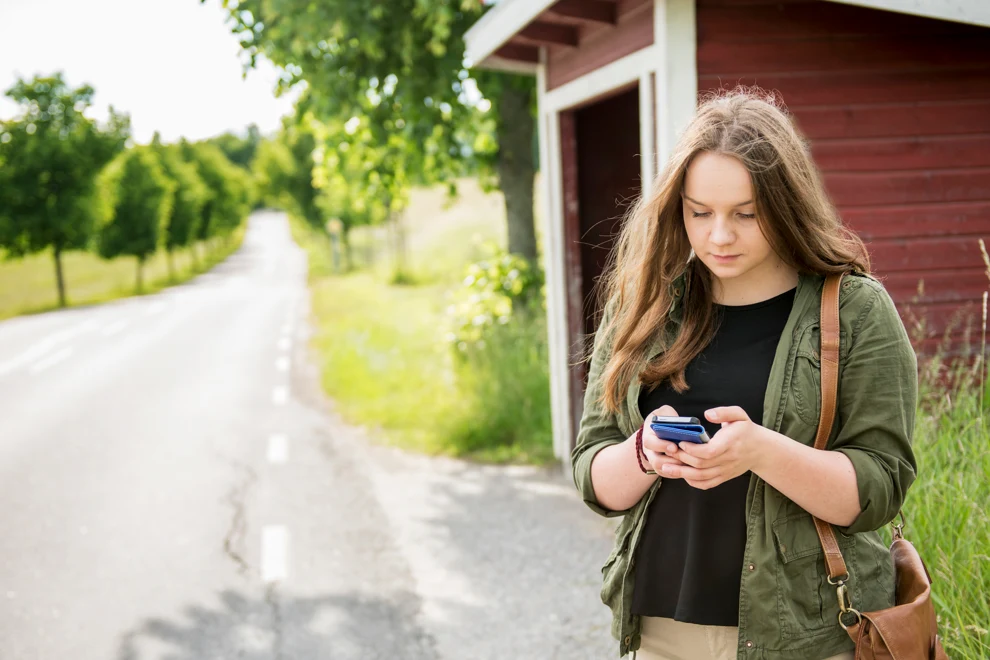 En kvinna som står vid en landsväg och tittar i sin mobil.