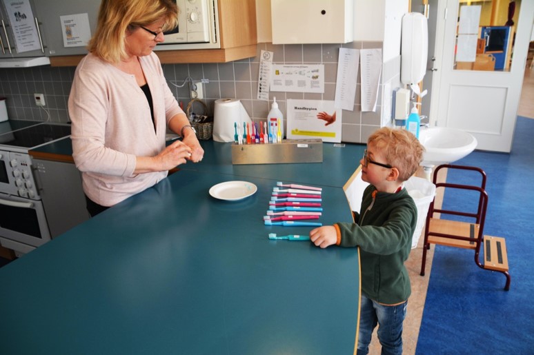 Ett barn och en pedagog på förskolan tittar på tandborstar och ett fat med tandkrämsklickar.